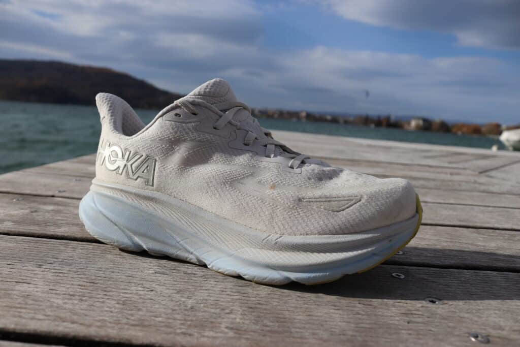 Picture of a silver pair of the Hoka Clifton 9 from the side at lake annecy