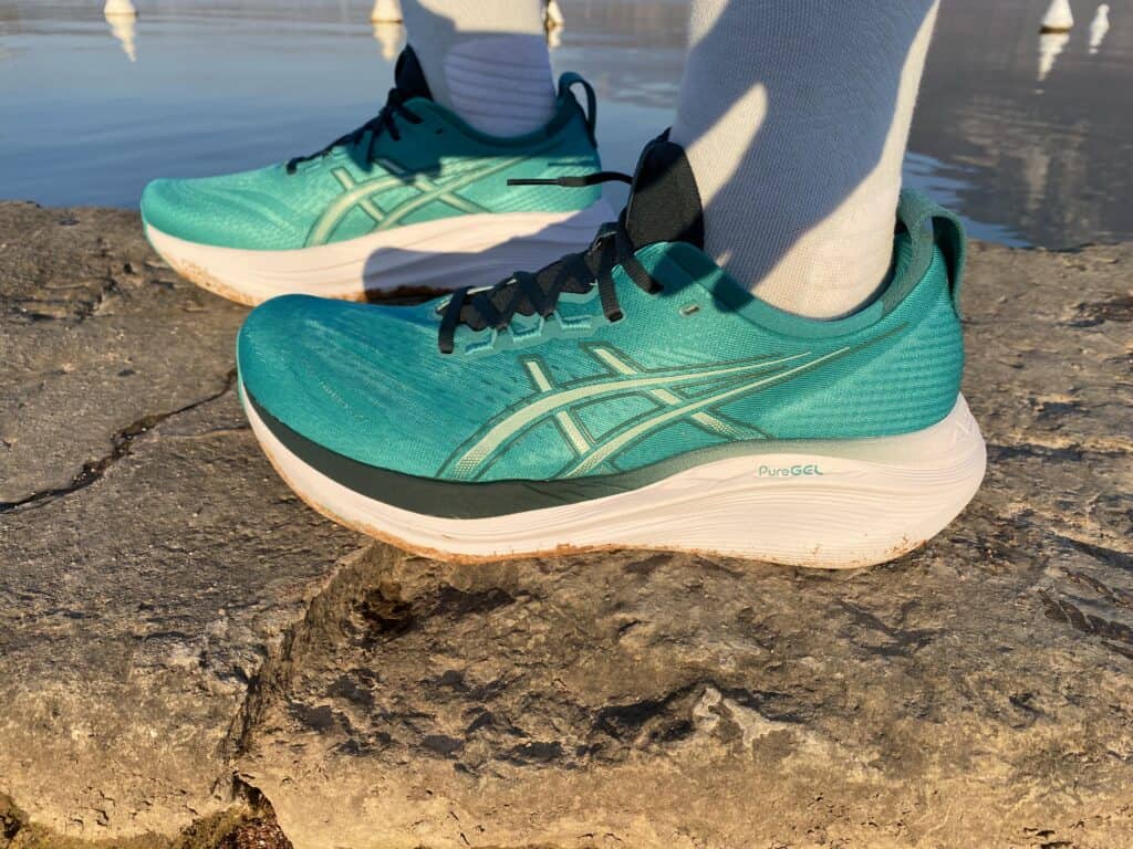 Picture from the side of james mccormack wearing the asics gel nimbus 27 in Wave Teal/Saxon Green at annecy lake