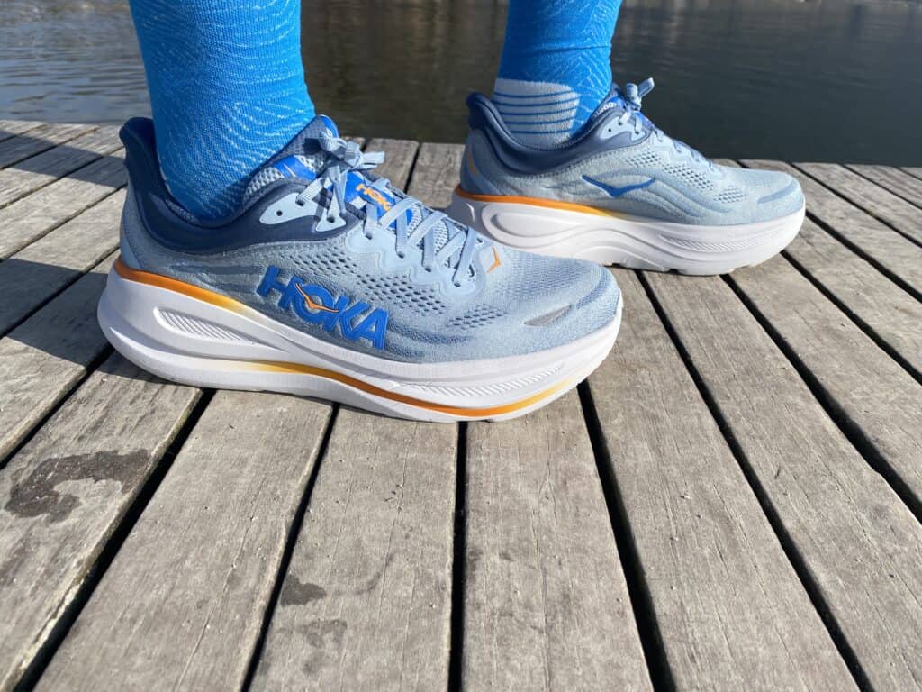 Picture of James Mccormack wearing the hoka bondi 9 with blue socks and you can see the shoes and the socks with annecy lake in the background